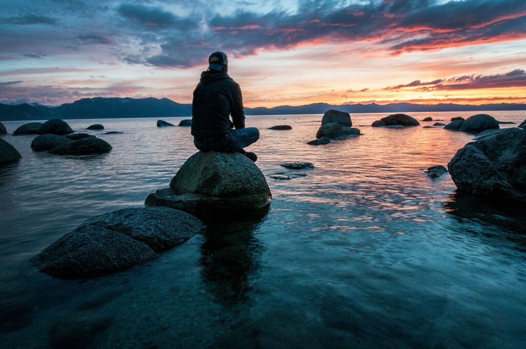 A person sitting on a rock looking out over calm water at sunset